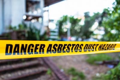 Caution tape that reads "DANGER ASBESTOS DUST HAZARD" surrounding a house.